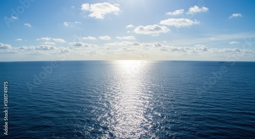 A serene view of the ocean under a bright blue sky with scattered clouds. Sunlight glimmers on the water, creating a tranquil atmosphere perfect for nature and relaxation projects.