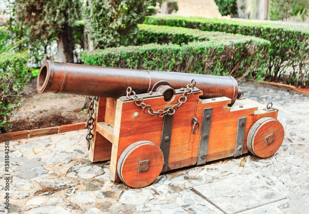 Historic iron cannon on a sturdy wooden carriage, maritime and fortress defense. Set on a stone pathway with lush greenery, it adds an authentic touch to historical and military-themed collections