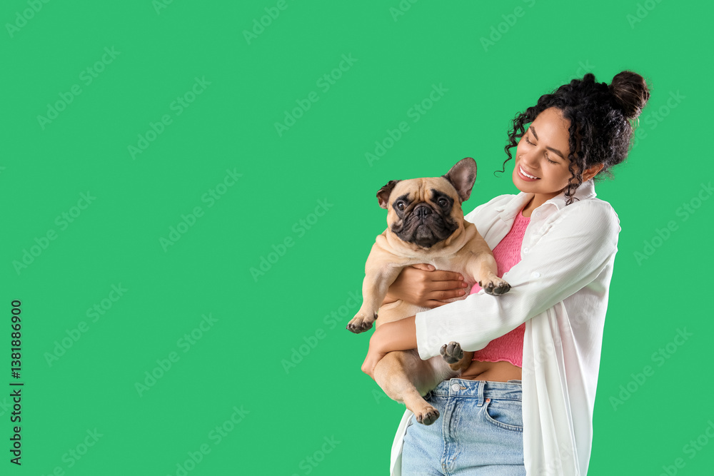 Happy young African-American woman with cute French bulldog on green background