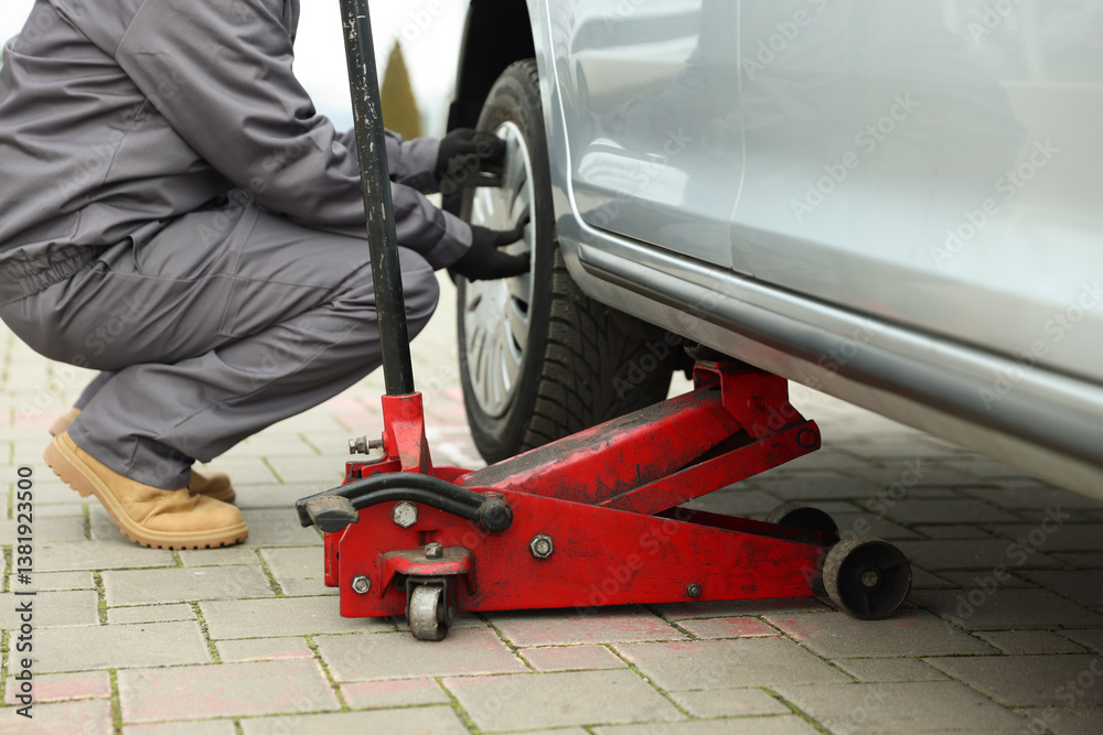 Fototapeta premium Car lifted by scissor jack. Auto mechanic changing wheel outdoors, closeup