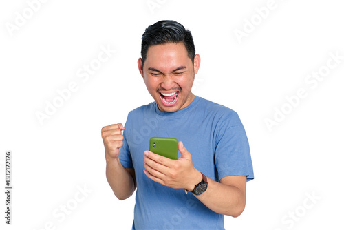 Excited young Asian man celebrating victory while looking at smartphone screen, holding phone and raising fist, isolated on transparent background photo