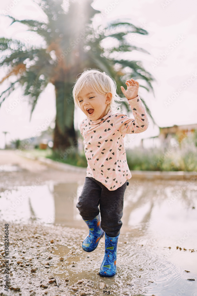 Naklejka premium Smiling little girl in rubber boots jumping on a puddle