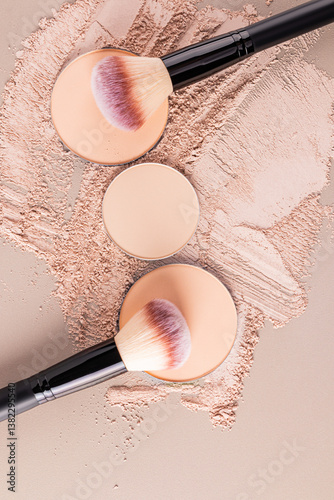 Three blocks of natural tone compact powder lie on top of a scattered beige tone dry mineral powder with two makeup brushes. The top vertical view.