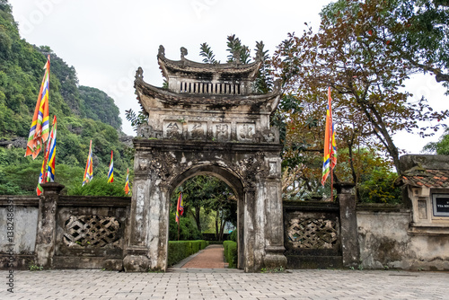 Two arched entrances flank a central ceremonial gate with flags and stone carvings in Ninh Bình, Vietnam on December 26, 2019