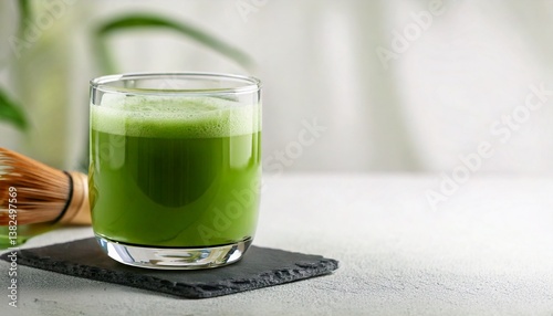 A bright green glass of matcha green tea is placed on a clean white surface. Matcha powder is sprinkled around it. It is perfect for use as a promotional image for health drinks or content related to 