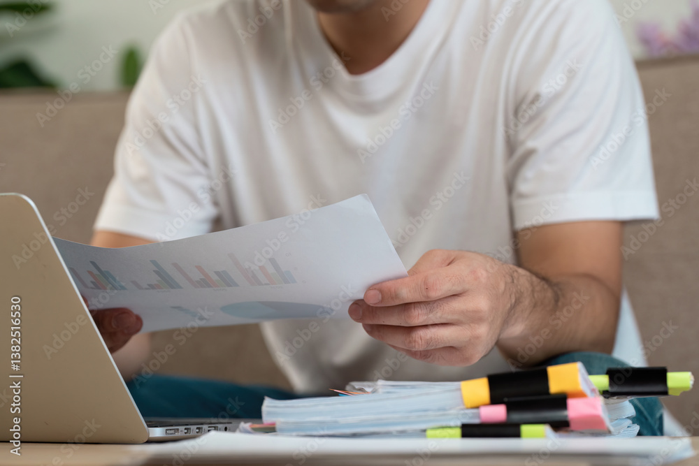 Business Analysis and Data Review. A man carefully reviewing financial reports while analyzing graphs and charts at home. Business Analysis and Data Review. A man carefully reviewing financial reports while analyzing graphs and charts at home.