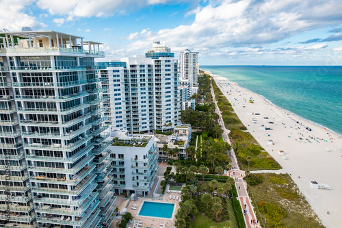 Miami Beach, Florida – Aerial photo shows modern beachfront condos with pools, green spaces, and a busy oceanfront boardwalk.
