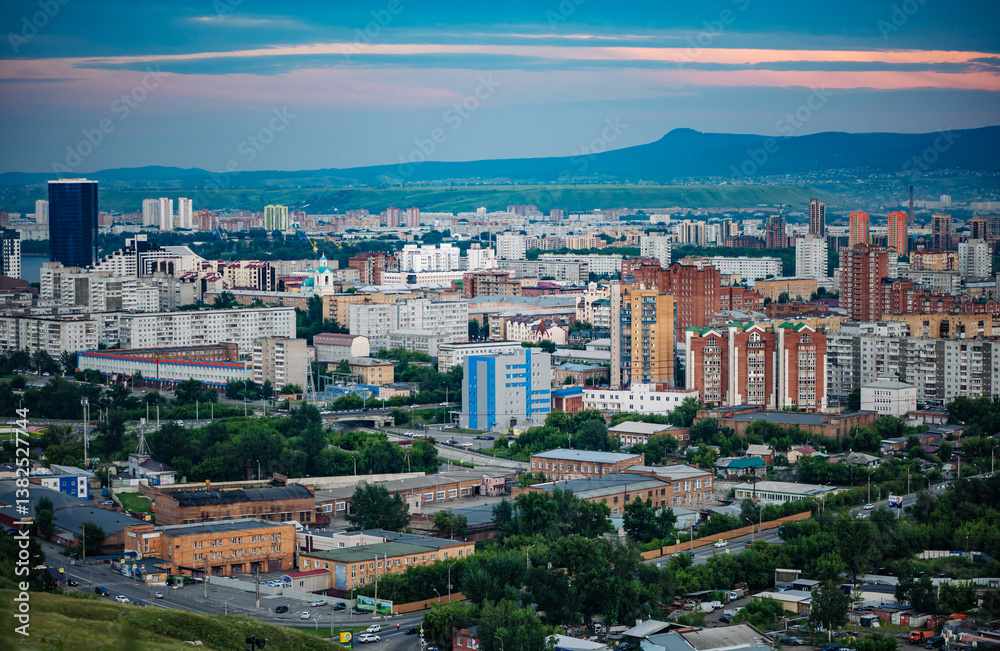 Fototapeta premium Krasnoyarsk cityscape revealing urban landscape, residential zones, winding streets, verdant greenery, mountain silhouettes against dramatic sunset lighting