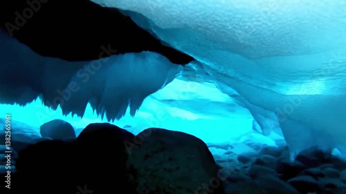 Breathtaking view of underwater ice cave with glowing blue light and rocky seafloor, frozen arctic tunnel, surreal natural formation, extreme cold environment exploration footage