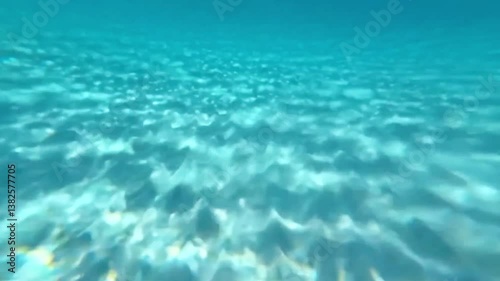 Sunlight refracting underwater on ocean floor, creating dynamic ripples and light patterns in crystal-clear blue water