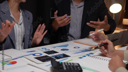 Business team working late in office, analyzing financial reports, charts, and graphs, discussing growth strategies and pointing at important data