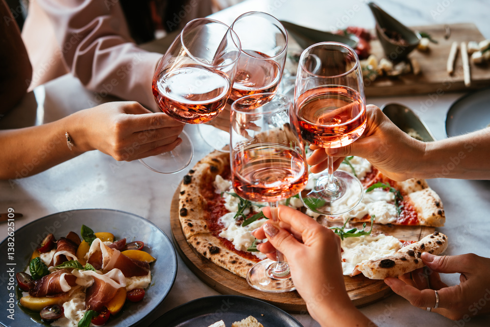 Friends enjoy a dinner party with pizza and rose wine in a bar or a restaurant.