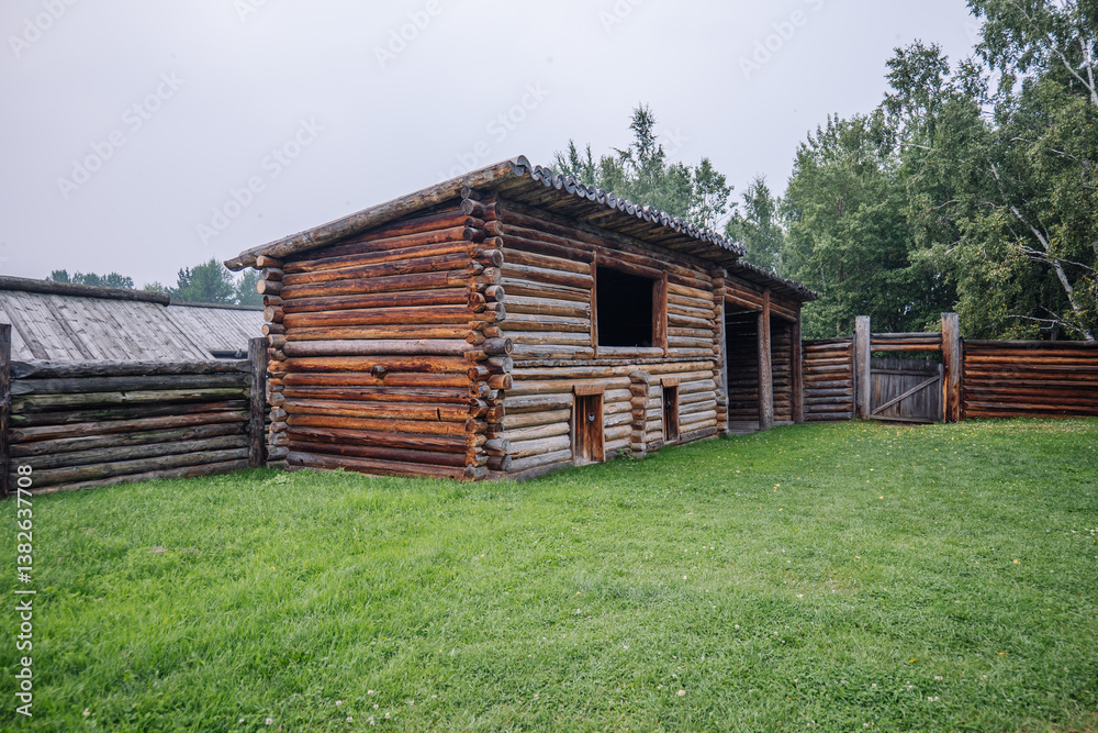 Old wooden barn with small doors and windows in a green field, surrounded by a wooden fence, in the russian countryside Old wooden barn with small doors and windows in a green field, surrounded by a wooden fence, in the russian countryside