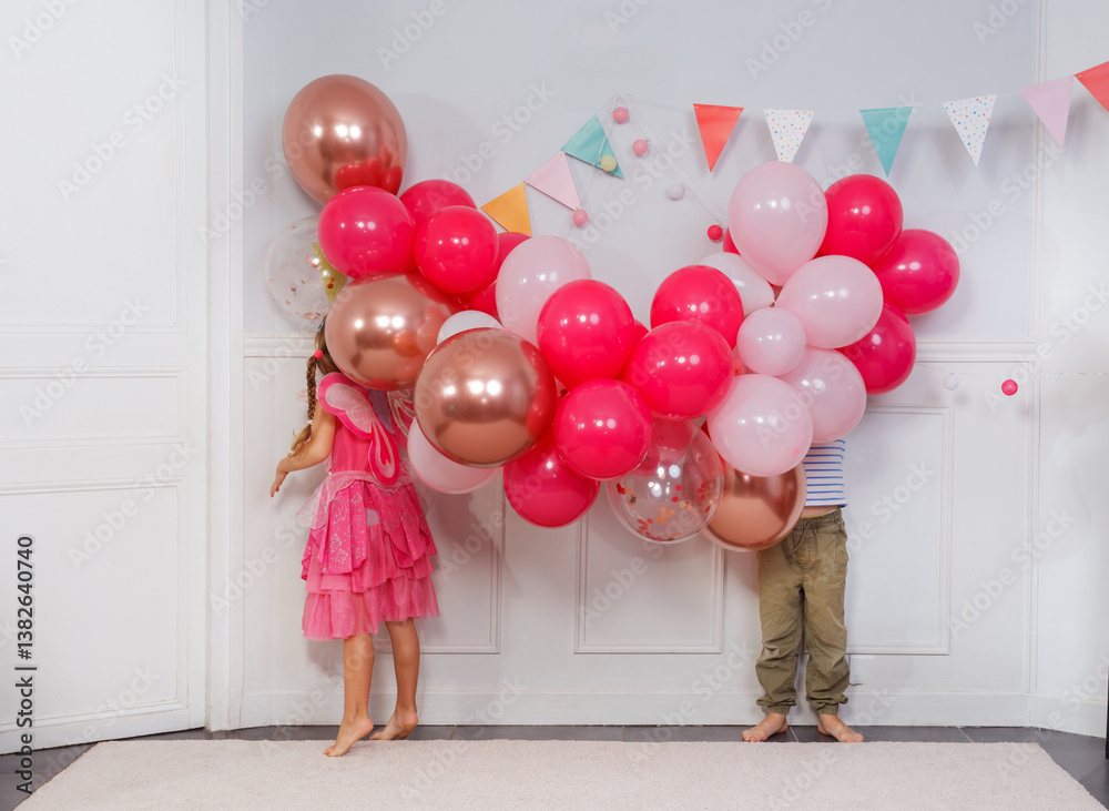 Funny kids hide heads in butch of bday balloons, concept image