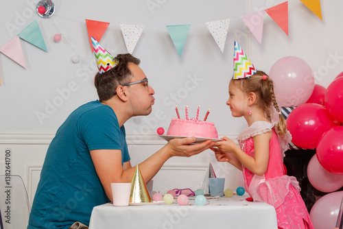 Dad with his daughter blow out candles on birthday party cake