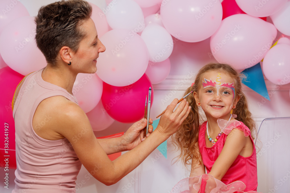 A girl beams with joy as an adult woman applies unicorn makeup