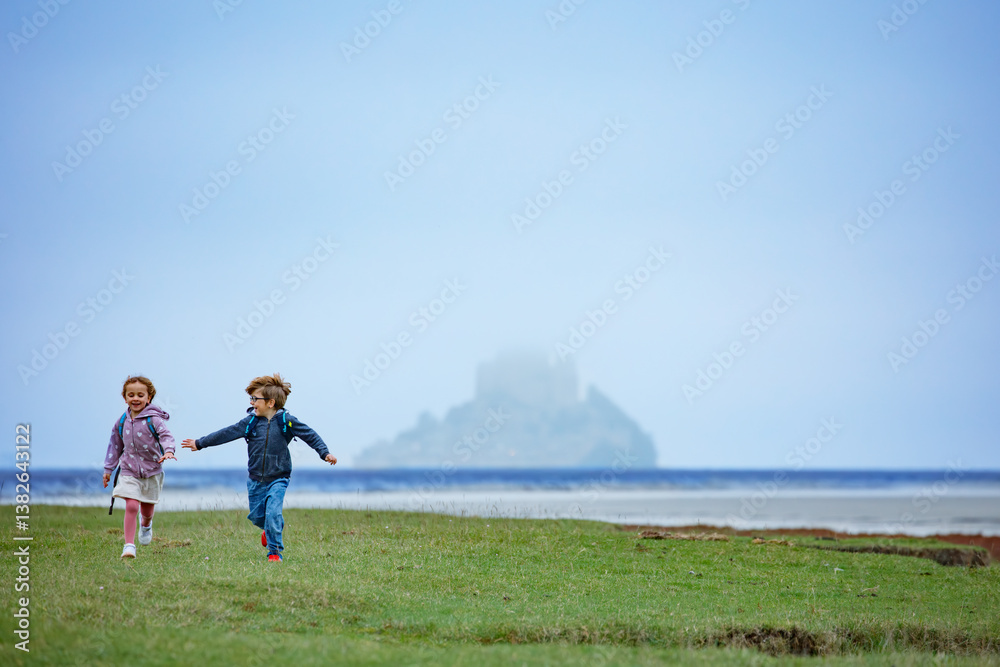 Boy and girl run on fields, Mont Saint Michel in misty distance