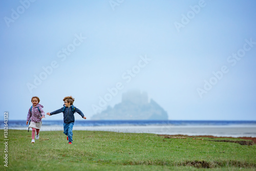 Boy and girl run on fields, Mont Saint Michel in misty distance