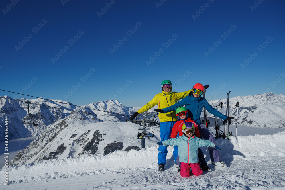 Four people pose with skis on a snowy mountain under clear skies