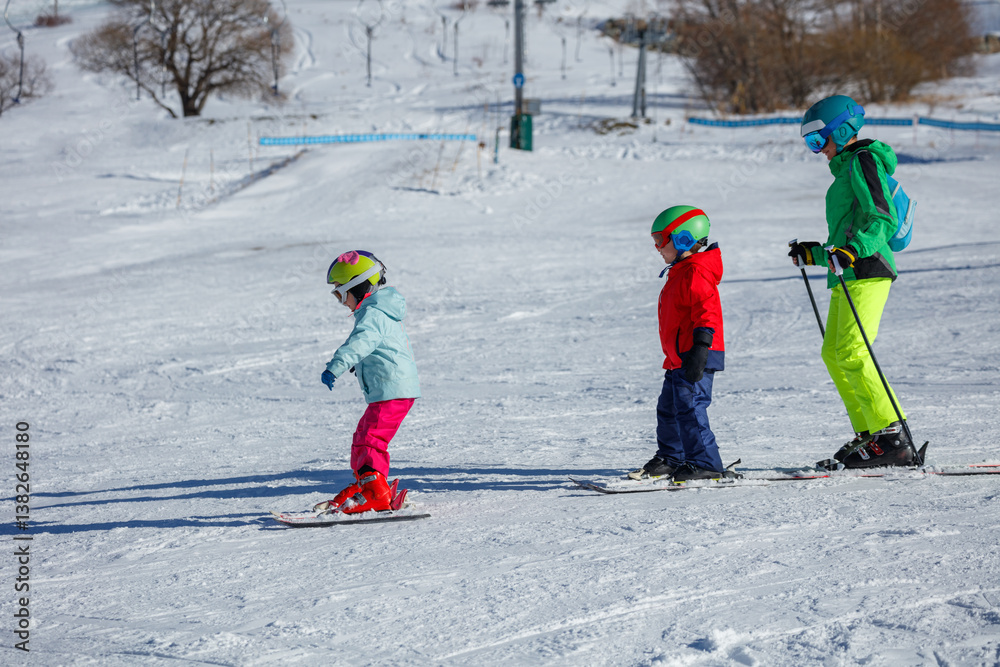 Children in bright ski outfits glide down a snow hill at resort