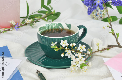 Obraz na płótnie Cup of tea or coffee and flowers on a table with light tablecloth. Writing implements, maybe someone is writing a letter or an invitation. w salonie