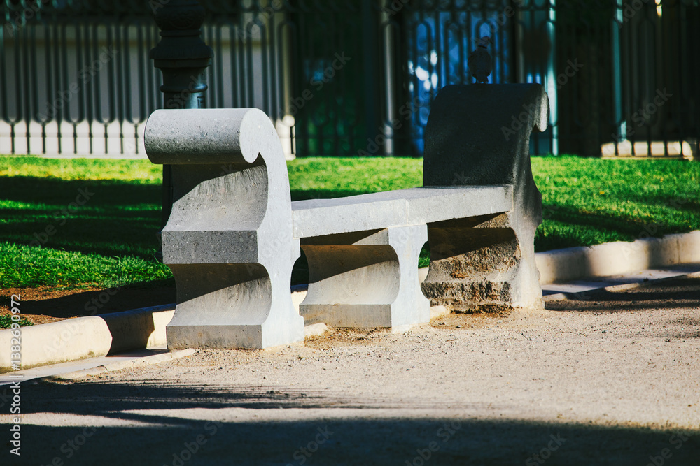 Weathered gray stone bench, nestled in a grassy park, casts long shadows in the afternoon sun. Ornate stone bench, a tranquil spot in a well-maintained park