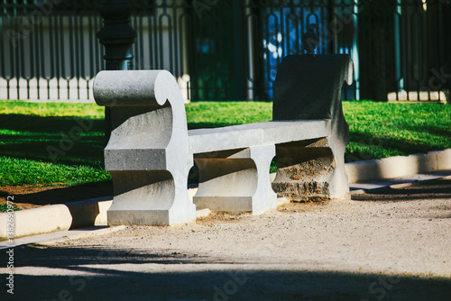 Obraz na płótnie Weathered gray stone bench, nestled in a grassy park, casts long shadows in the afternoon sun. Ornate stone bench, a tranquil spot in a well-maintained park w salonie