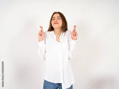 Caucasian young girl wearing white shirt  gesturing finger crossed smiling with hope and eyes closed. Luck and superstitious concept.