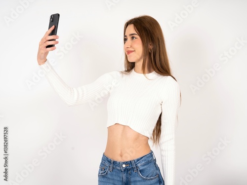 Caucasian young girl wearing white T-shirt smiling and taking a selfie ready to post it on her social media.