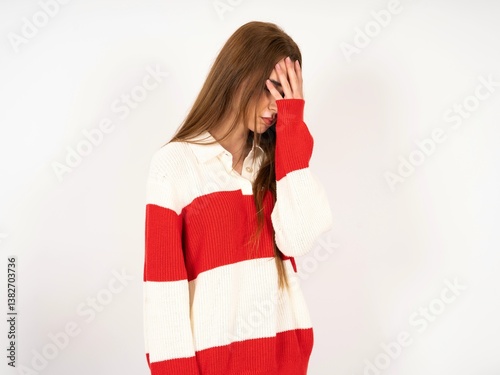 Caucasian young girl wearing striped sweater with sad expression covering face with hands while crying. Depression concept.