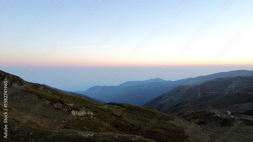 Fototapeta premium A drone shot at dawn in the mountains of Georgia. View of the hills, forest and Mount Ararat. A small, cozy, red forest ranger's house in the mountains