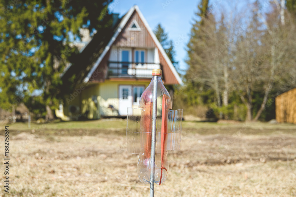 An empty upside-down plastic bottle with cut-off blades spins,vibrates and rattles in the garden, scaring away moles and water voles. Selective focus on homemade windmill, cute small house on back. An empty upside-down plastic bottle with cut-off blades spins,vibrates and rattles in the garden, scaring away moles and water voles. Selective focus on homemade windmill, cute small house on back.
