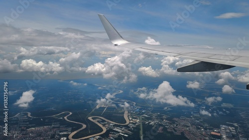 Aerial View from Airplane Window Showing Wing, Curving River, Cloud Formations, and Cityscape Below on a Bright Day