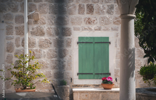 Stone wall of a Mediterranean house with a window with shutters and potted plants