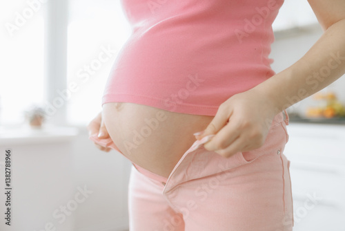 Expecting mother adjusting her clothing in a bright kitchen setting