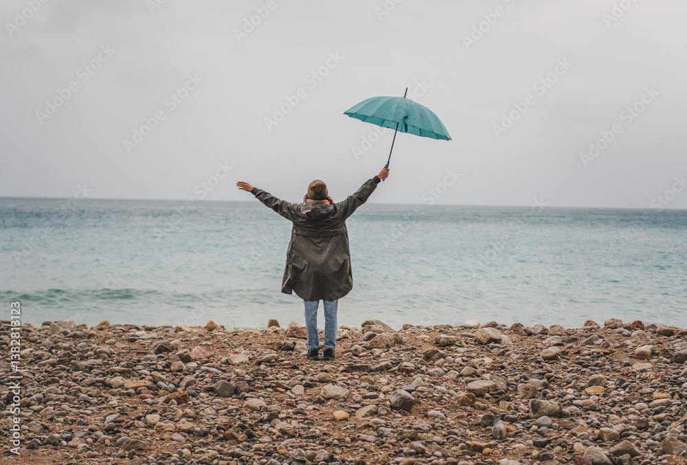 Young woman walking in the rain with a blue umbrella on the seashore