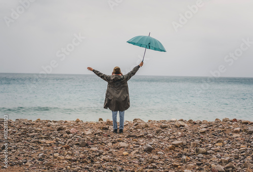 Obraz na płótnie Young woman walking in the rain with a blue umbrella on the seashore w salonie