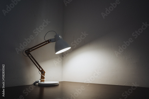 A stylish desk lamp is prominently sitting on a wooden table in an otherwise dark room, casting soft light and creating intriguing shadows that enhance the atmosphere within the space