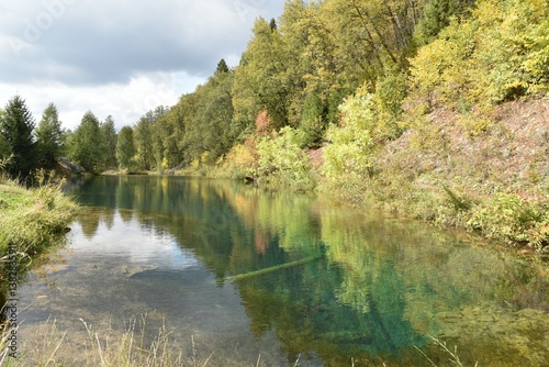 Tranquil river reflecting autumn colors in a forested area during a cloudy afternoon
