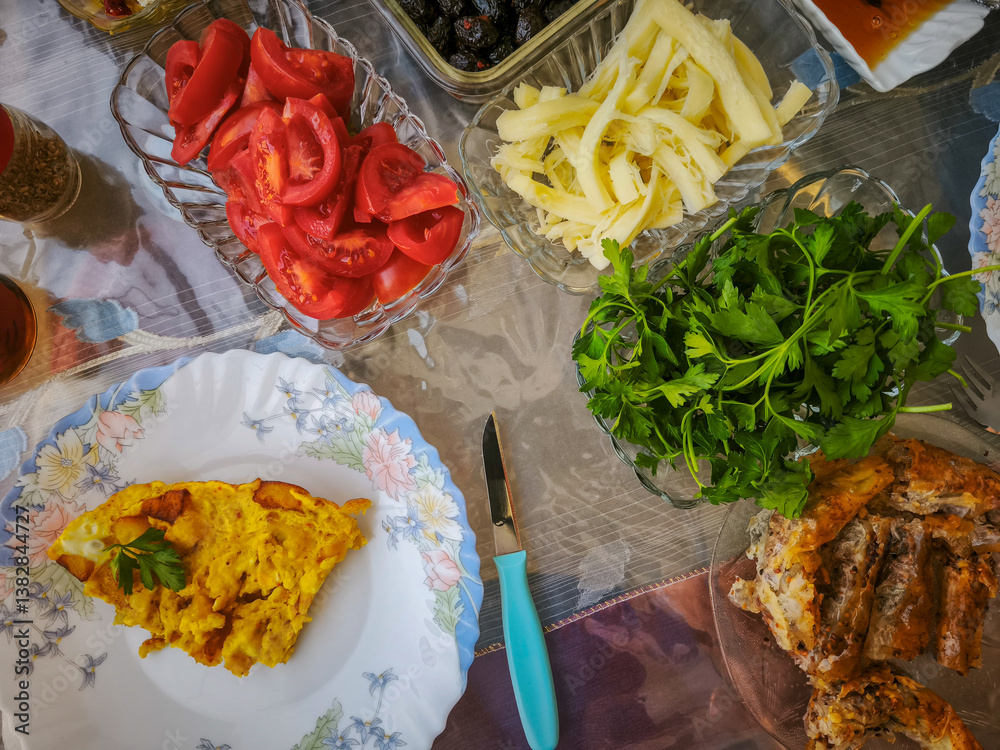 Turkish breakfast table. Flat-lay of peoples hands taking pastries, vegetables, greens, olives, cheeses, fried eggs, spices, jams, honey, tea in copper pot and tulip glasses, wide composition