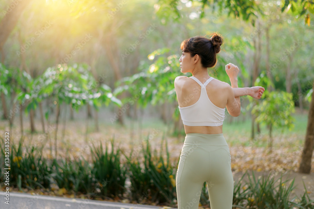 Fototapeta premium asian woman stretching before workout outdoors in park, enjoying fresh air and sunlight in serene natural setting. sport, wellness and healthy lifestyle concept