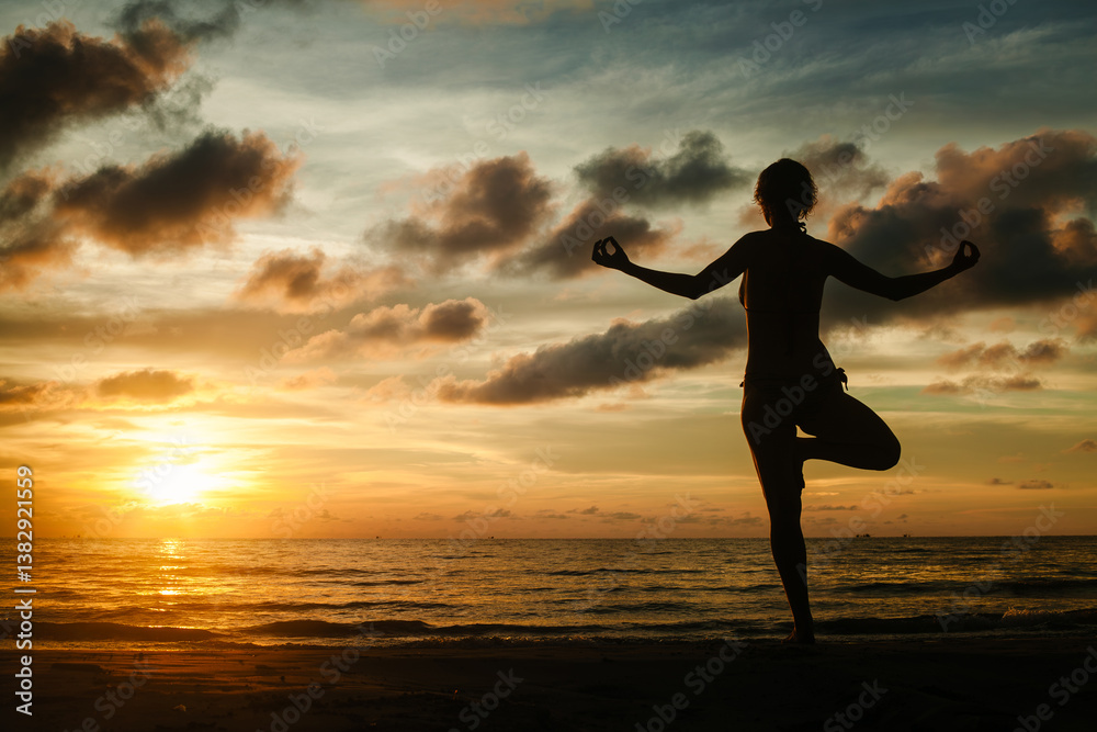 The silhouette of a woman practicing yoga on a tropical beach during a magical sunset.