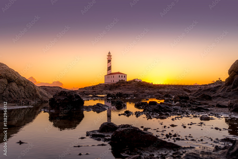 A breathtaking sunset view of lighthouse of Favaritx, Menorca, casting a warm glow over the iconic lighthouse and its rocky surroundings. Minorca Iconic Lighthouse at Dusk.