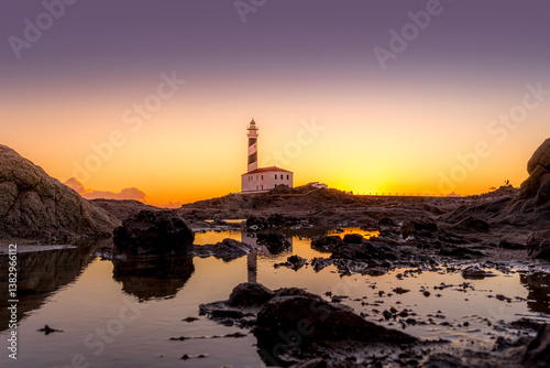 Obraz na płótnie A breathtaking sunset view of lighthouse of Favaritx, Menorca, casting a warm glow over the iconic lighthouse and its rocky surroundings. Minorca Iconic Lighthouse at Dusk. w salonie