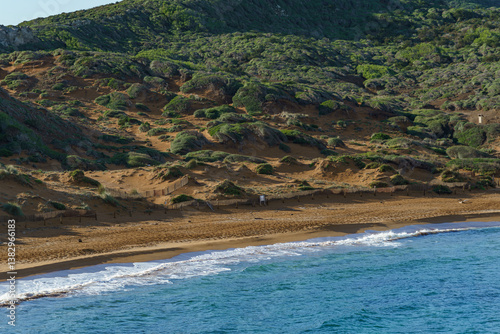 Obraz na płótnie A stunning aerial view of Cavalleria Beach in Menorca, showcasing its natural beauty where sandy shores meet the turquoise Mediterranean Sea, bordered by a lush green hillside w salonie
