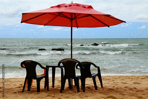 Vacations in summer tropical beach. SEa warm water breaking on the beach, red parasol and black chairs on the shore. Moments for relaxing in open wide seascape environment