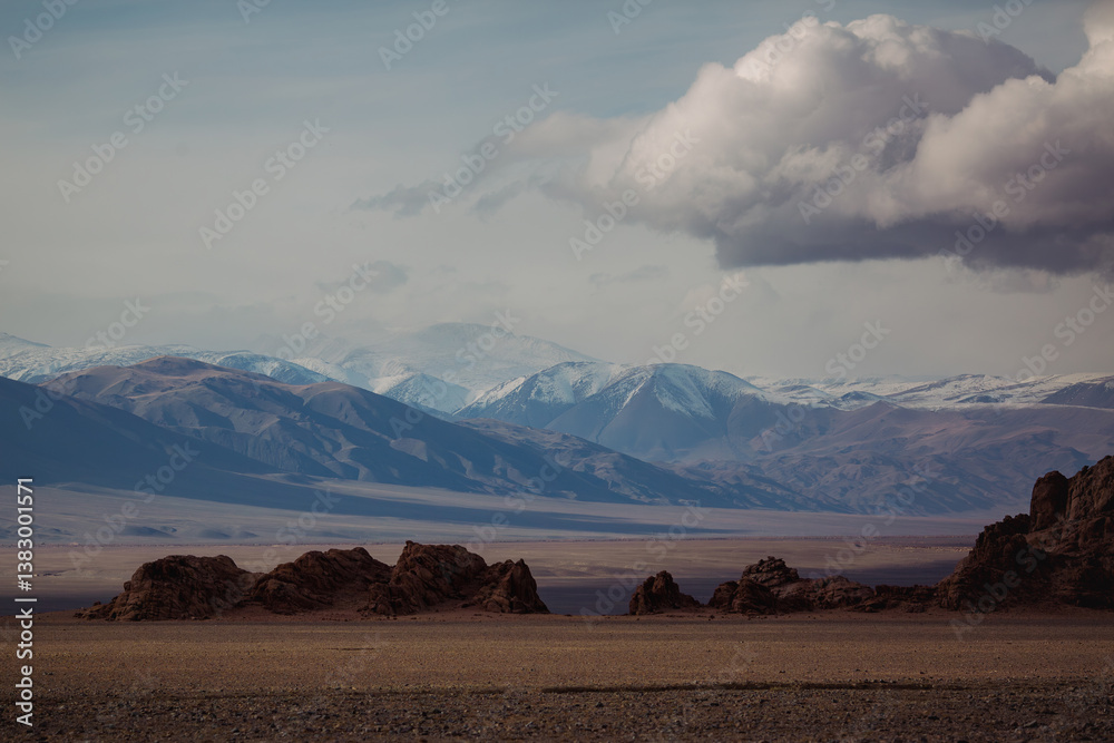 A rugged landscape with snow-capped peaks fading into the blue sky in Mongolia, embodying raw beauty and vastness.