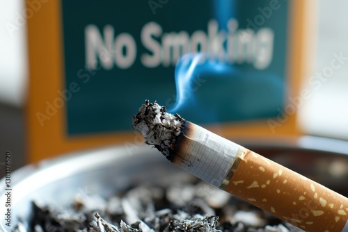 A lit cigarette smolders in an ashtray while a 'No Smoking' sign is prominently displayed in the background, provoking thoughts on smoking habits and public health.