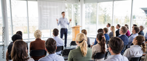 A bright modern conference room with floor to ceiling windows along the back wall A speaker stands at the front of the room