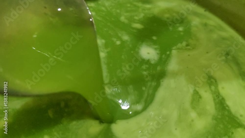 a close-up scene of green liquid foodstuffs being stirred with a spoon in a stainless steel container. 